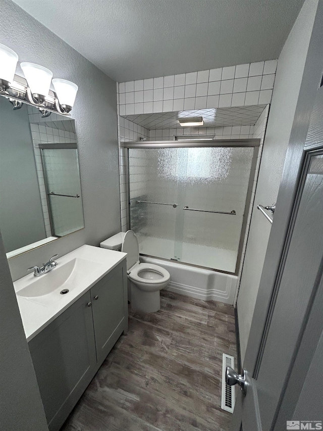 full bathroom featuring hardwood / wood-style flooring, enclosed tub / shower combo, vanity, toilet, and a textured ceiling