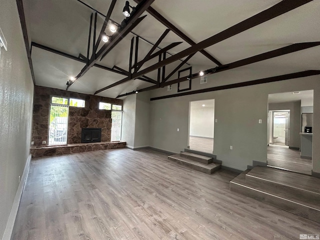 unfurnished living room with hardwood / wood-style flooring, a stone fireplace, high vaulted ceiling, and beam ceiling