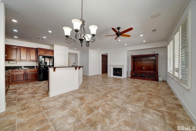 kitchen with pendant lighting, a breakfast bar, ceiling fan with notable chandelier, black fridge, and ornamental molding