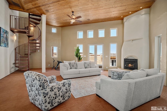 living room with wooden ceiling, a high ceiling, carpet floors, a wood stove, and ceiling fan