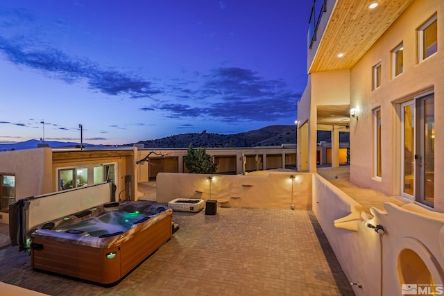 patio terrace at dusk featuring a hot tub and a mountain view