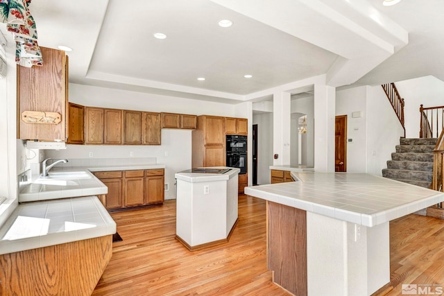 kitchen featuring tile counters, a center island, sink, double oven, and light hardwood / wood-style floors