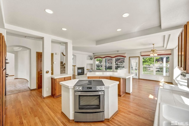 kitchen featuring a tray ceiling, light countertops, open floor plan, stainless steel range with electric cooktop, and light wood-type flooring