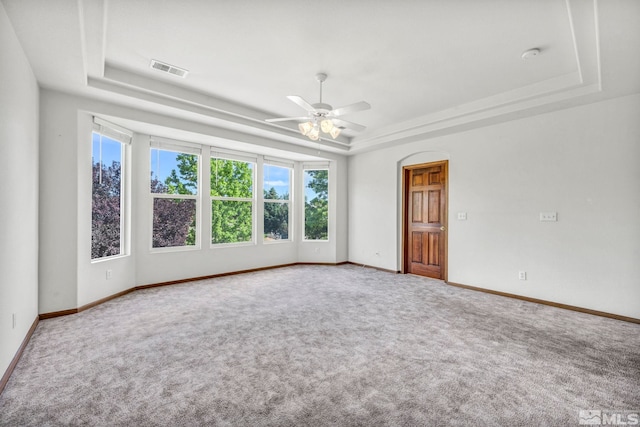 empty room featuring visible vents, baseboards, a raised ceiling, a ceiling fan, and carpet floors