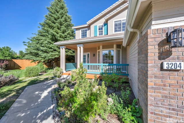 doorway to property featuring a porch, brick siding, and fence