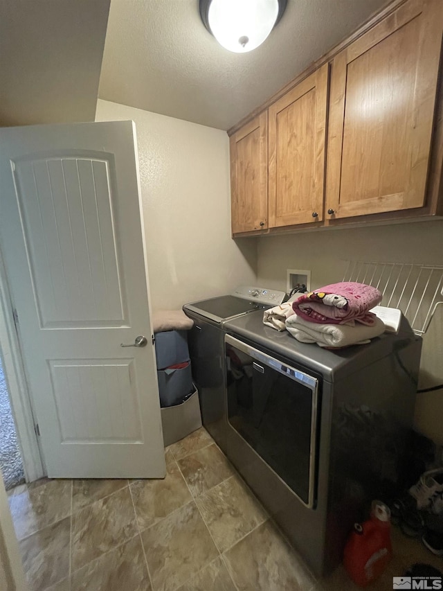 washroom with washing machine and clothes dryer, cabinets, and a textured ceiling