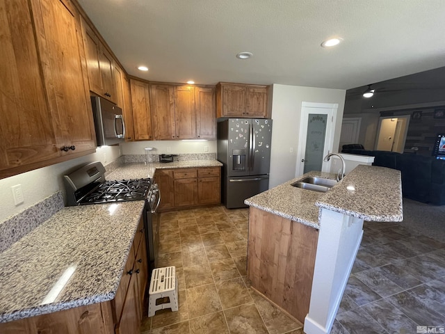 kitchen with a kitchen island with sink, a kitchen breakfast bar, sink, light stone countertops, and appliances with stainless steel finishes