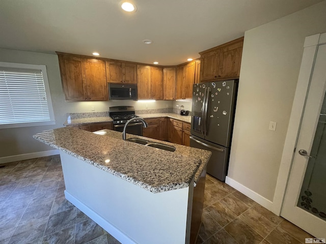 kitchen with light stone countertops, sink, an island with sink, and stainless steel appliances