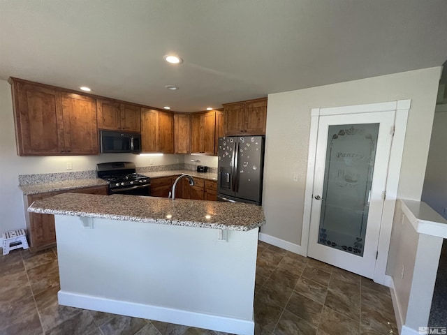 kitchen with stone counters, sink, a kitchen breakfast bar, an island with sink, and black appliances