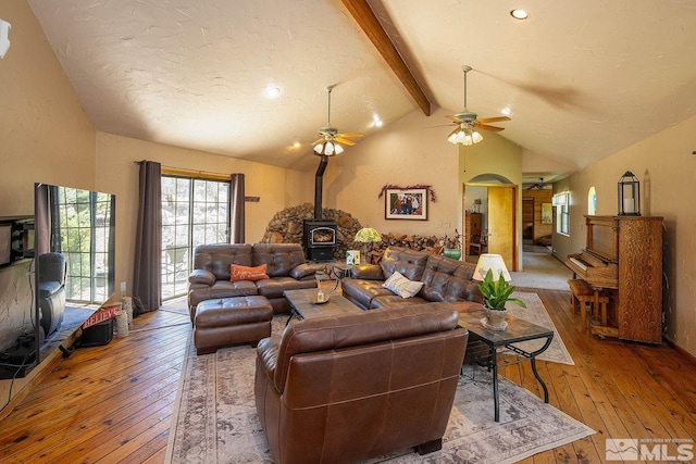 living room featuring lofted ceiling with beams, light hardwood / wood-style floors, a wood stove, and ceiling fan