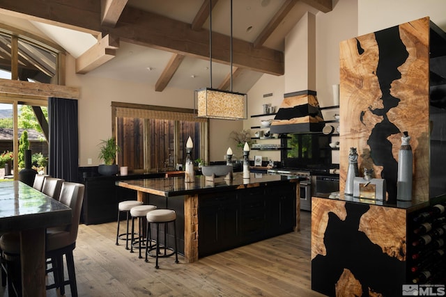 kitchen featuring a breakfast bar area, light hardwood / wood-style floors, vaulted ceiling with beams, and high end range