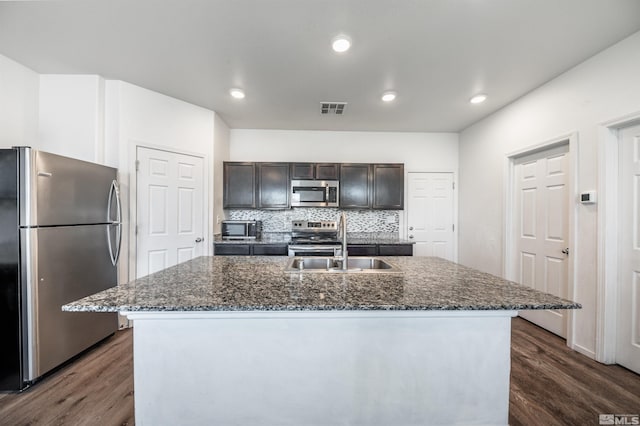 kitchen featuring hardwood / wood-style flooring, tasteful backsplash, appliances with stainless steel finishes, and an island with sink