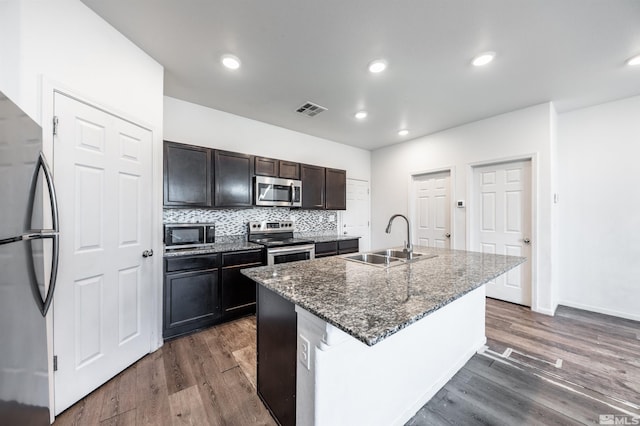 kitchen with dark hardwood / wood-style flooring, appliances with stainless steel finishes, sink, and an island with sink