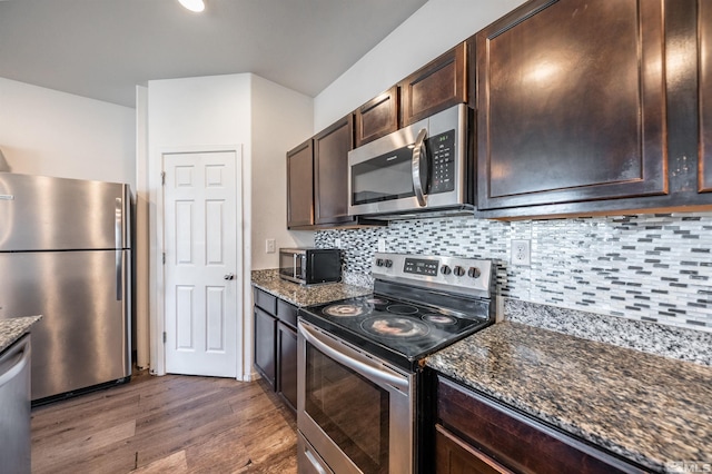 kitchen with decorative backsplash, dark hardwood / wood-style floors, dark stone counters, and appliances with stainless steel finishes