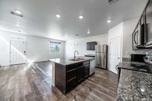 kitchen featuring appliances with stainless steel finishes, stone counters, sink, an island with sink, and dark wood-type flooring