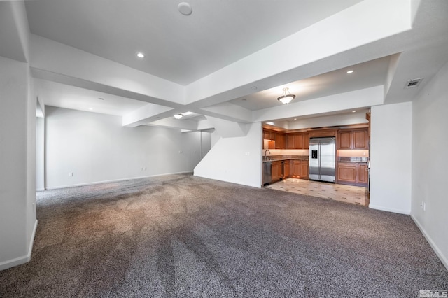 unfurnished living room featuring a tray ceiling, sink, and light colored carpet