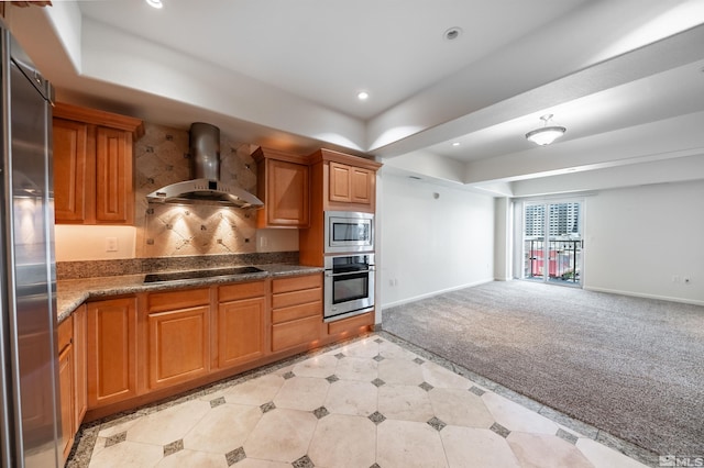 kitchen with appliances with stainless steel finishes, wall chimney exhaust hood, light carpet, and a tray ceiling