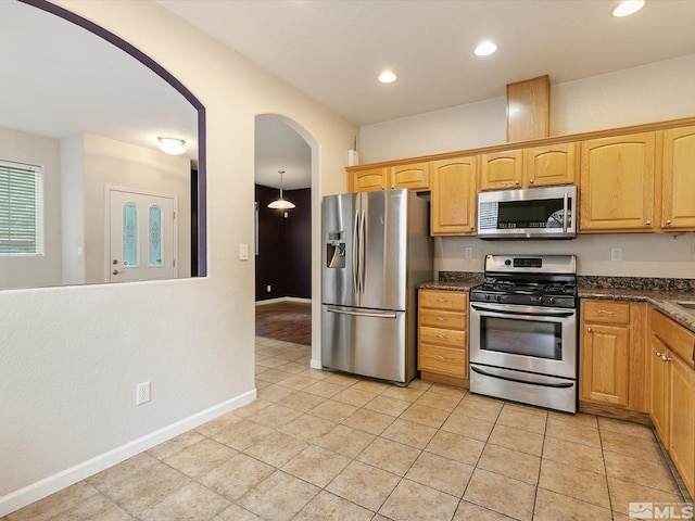 kitchen with light tile patterned flooring, dark stone counters, decorative light fixtures, and appliances with stainless steel finishes