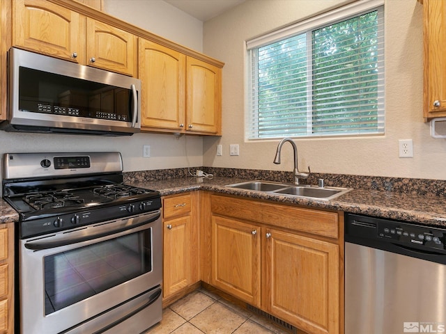 kitchen featuring appliances with stainless steel finishes, light tile patterned floors, dark stone counters, and sink