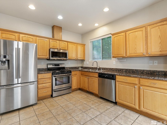 kitchen featuring appliances with stainless steel finishes, light tile patterned floors, dark stone countertops, and sink