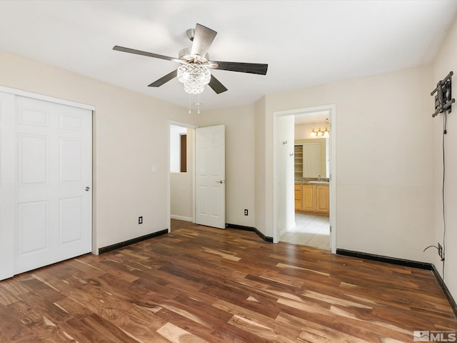 unfurnished bedroom featuring dark hardwood / wood-style flooring, ceiling fan with notable chandelier, and connected bathroom