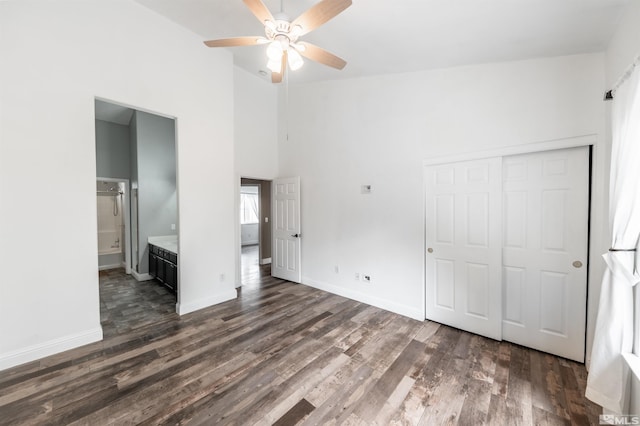 unfurnished bedroom featuring ceiling fan, dark wood-type flooring, high vaulted ceiling, connected bathroom, and a closet