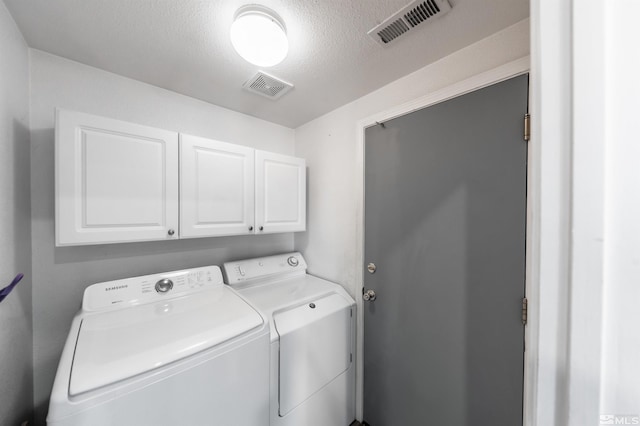 laundry area with washing machine and dryer, cabinets, and a textured ceiling