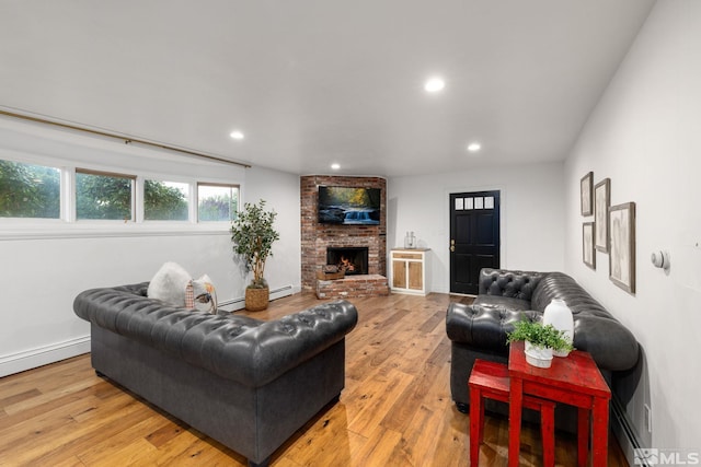 living room with light wood-type flooring, a brick fireplace, and a baseboard heating unit