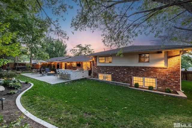 back house at dusk featuring a lawn, exterior bar, and a patio