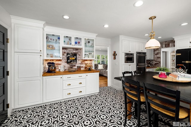 kitchen with wooden counters, stainless steel double oven, white cabinetry, and black refrigerator