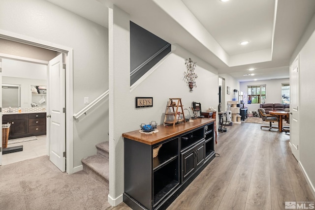 hallway with sink, a tray ceiling, and light hardwood / wood-style floors