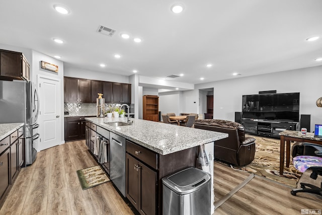 kitchen with sink, a kitchen island with sink, stainless steel appliances, dark brown cabinetry, and light hardwood / wood-style floors