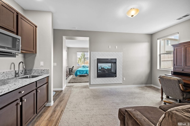 kitchen with sink, dark brown cabinets, a fireplace, and light wood-type flooring