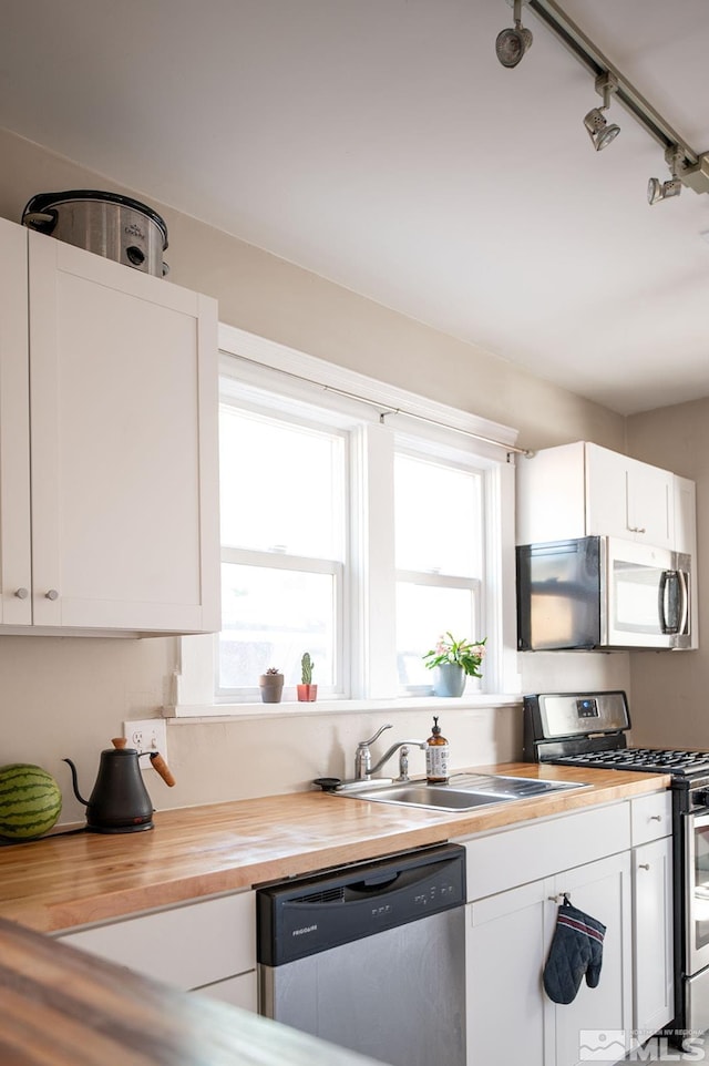 kitchen with sink, white cabinets, track lighting, and stainless steel appliances