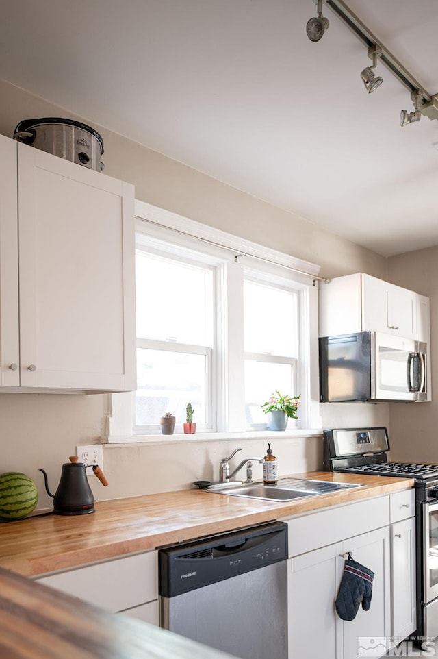 kitchen with stainless steel appliances, white cabinetry, a sink, and wood counters