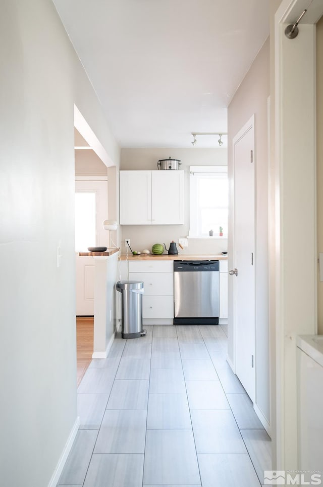 kitchen with light tile patterned floors, baseboards, white cabinets, dishwasher, and light countertops