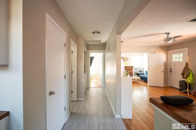 corridor with light wood-type flooring, visible vents, and baseboards