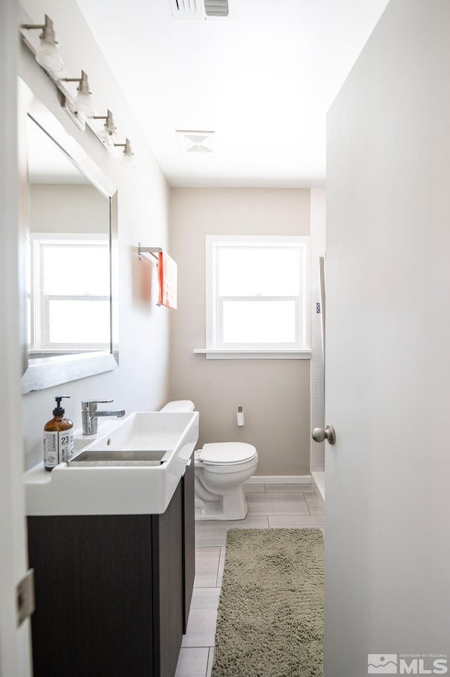 bathroom with a healthy amount of sunlight, tile flooring, vanity, and toilet