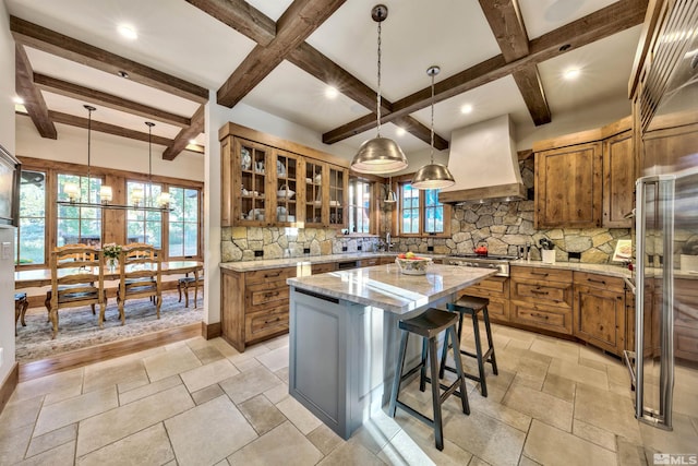 kitchen with pendant lighting, a kitchen island, light stone counters, and premium range hood