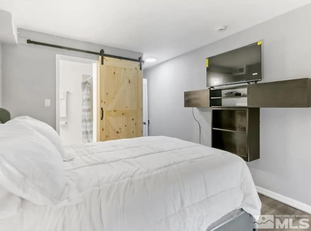 bedroom featuring connected bathroom, a barn door, and dark wood-type flooring