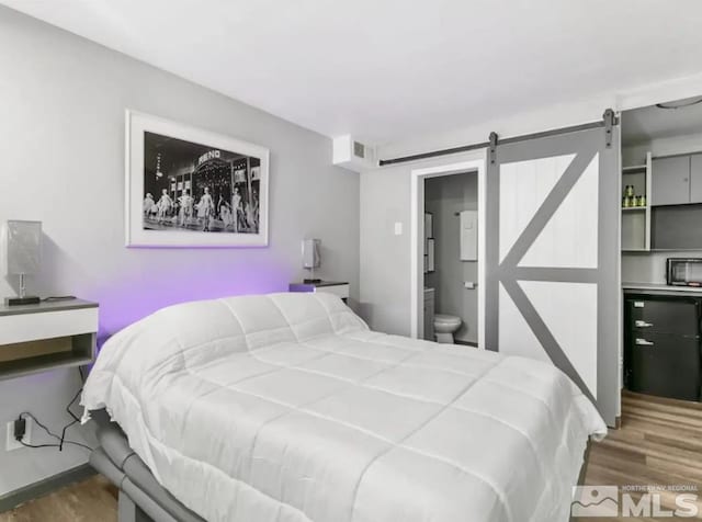 bedroom with dark hardwood / wood-style floors, a barn door, and ensuite bathroom