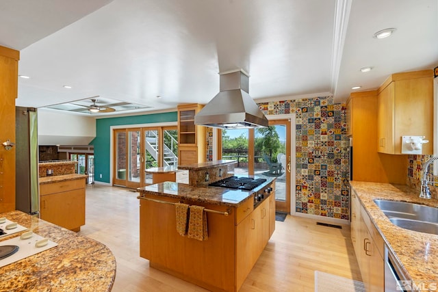 kitchen featuring sink, a center island, light stone counters, island range hood, and appliances with stainless steel finishes