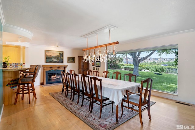 dining area with light hardwood / wood-style floors, ornamental molding, and a chandelier