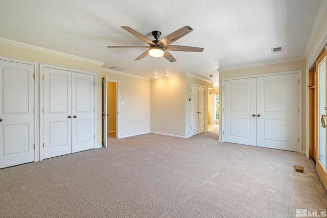 unfurnished bedroom featuring multiple closets, ceiling fan, light carpet, and ornamental molding