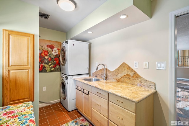 laundry area featuring light tile patterned floors, stacked washer and clothes dryer, and sink