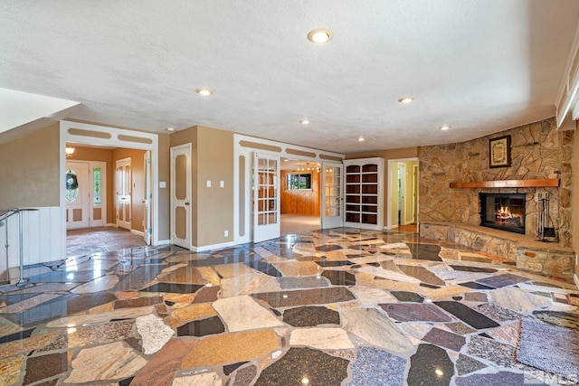 living room with french doors, a textured ceiling, and a stone fireplace