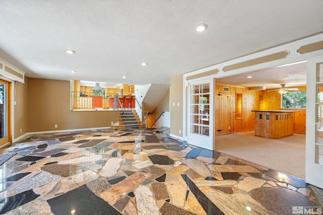 interior space featuring a textured ceiling, carpet floors, ceiling fan, and wooden walls