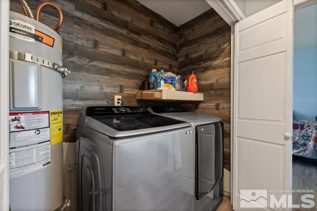 clothes washing area with washing machine and clothes dryer, wooden walls, and secured water heater