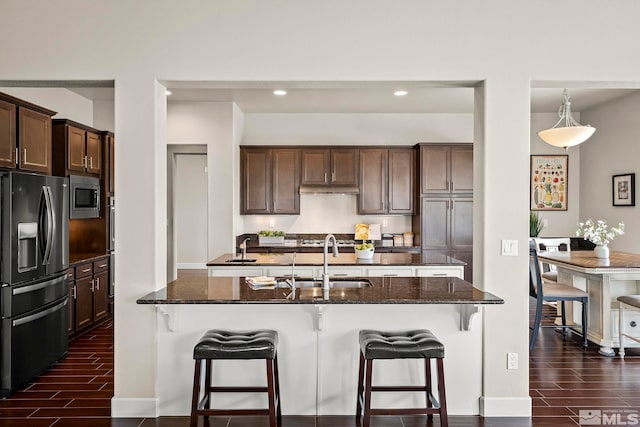 kitchen featuring dark hardwood / wood-style flooring, sink, dark stone countertops, appliances with stainless steel finishes, and a kitchen island with sink