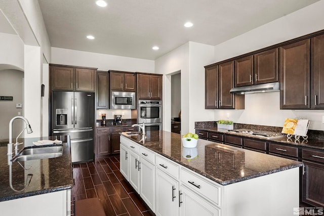 kitchen featuring under cabinet range hood, a sink, appliances with stainless steel finishes, wood tiled floor, and an island with sink